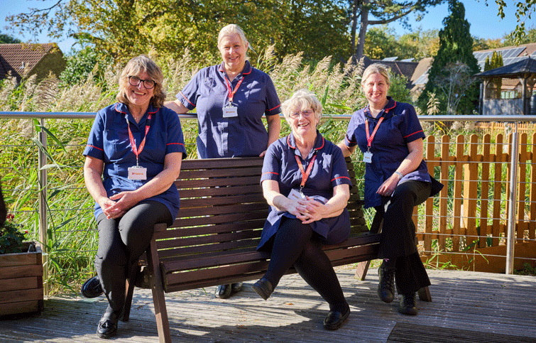 Image: clinical nurse specialists sitting on the decking by the pond at St Helena Hospice