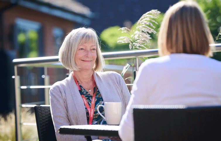 A counsellor is listening to another person, the image is taken from over their shoulder.