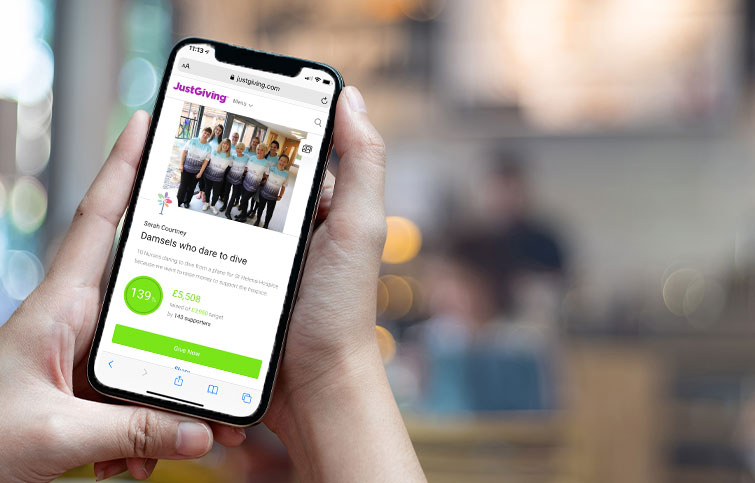 Someone holding a mobile phone displaying a JustGiving online fundraising page